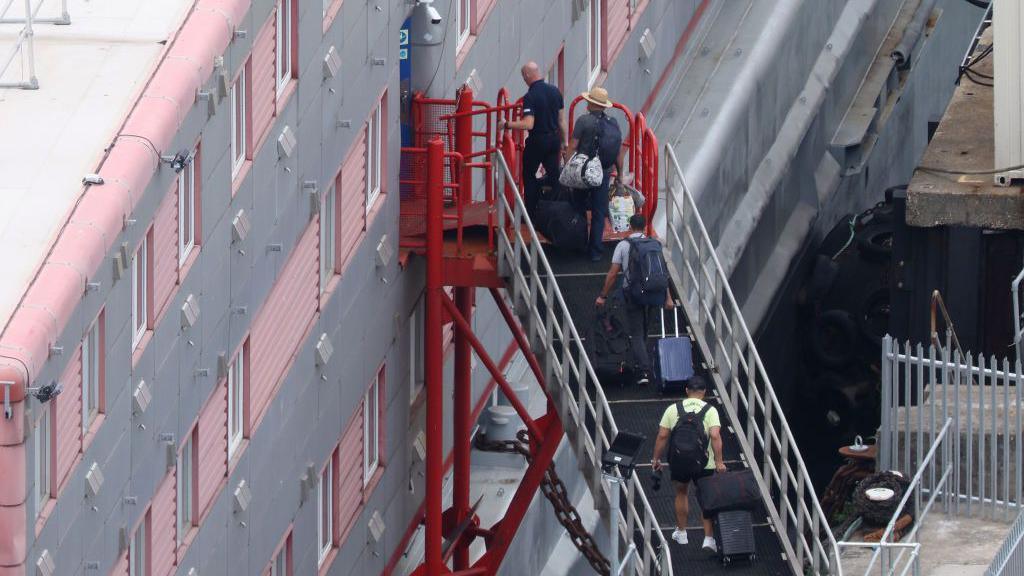 Men holding suitcases climbing a set of steps to board a barge