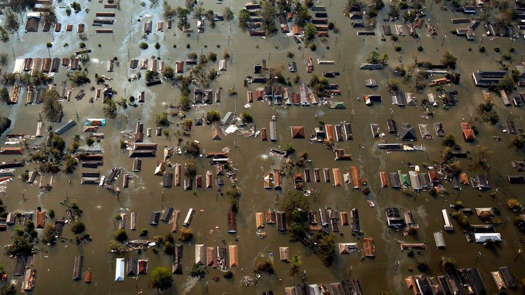 An aerial shot of dozens of buildings submerged under brown, murky water. numerous trees can also be seen. 