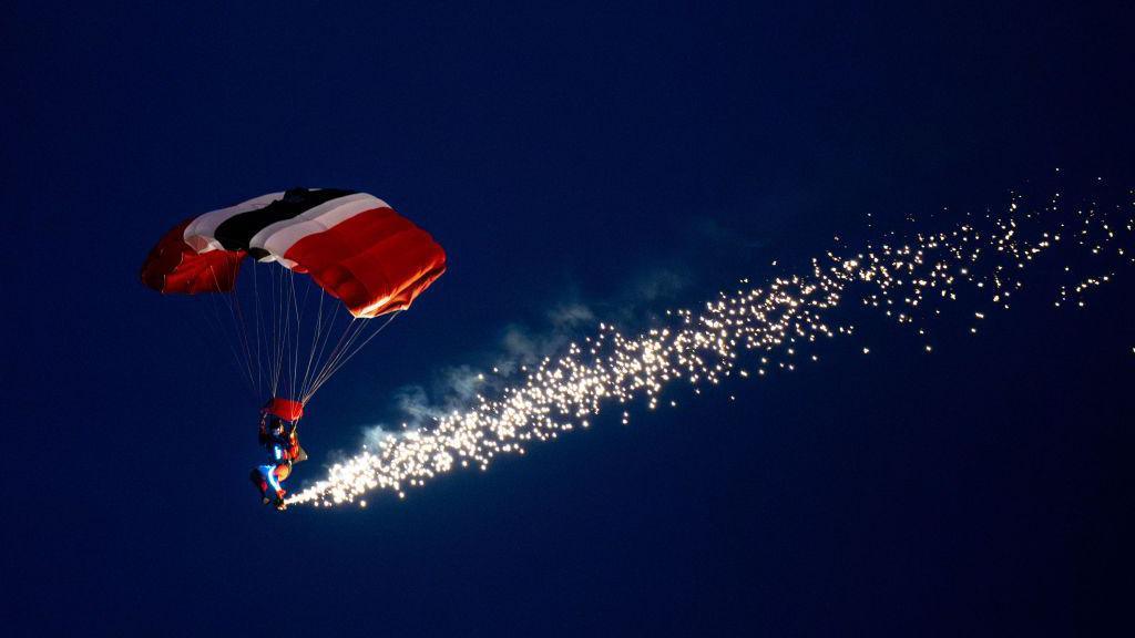 A parachutist with a red parachute in a dark sky with sparks coming from his feet