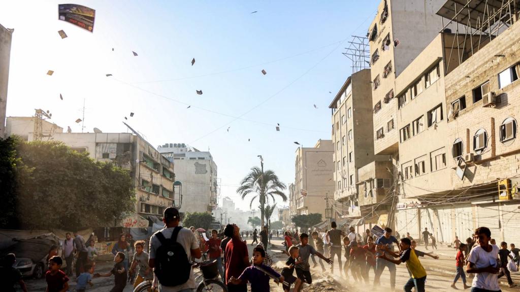 Leaflets fall over Gaza City as residents run around the streets.