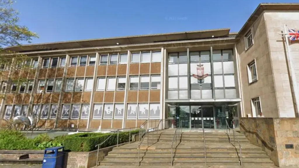 A large three-storey building, approached by wider steps to the main entrance. There is a large crest above the glazed entrance.