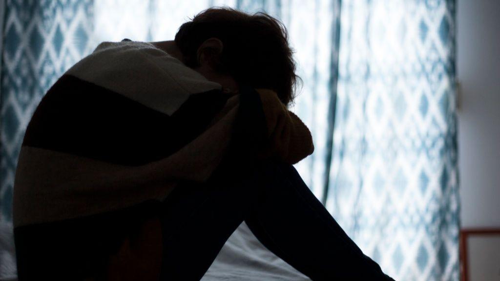 A silhouette of a woman sitting on a bed.  Her head is looking down. 