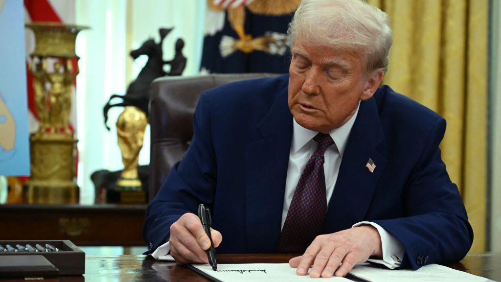 President Trump signing an executive order in the Oval Office.