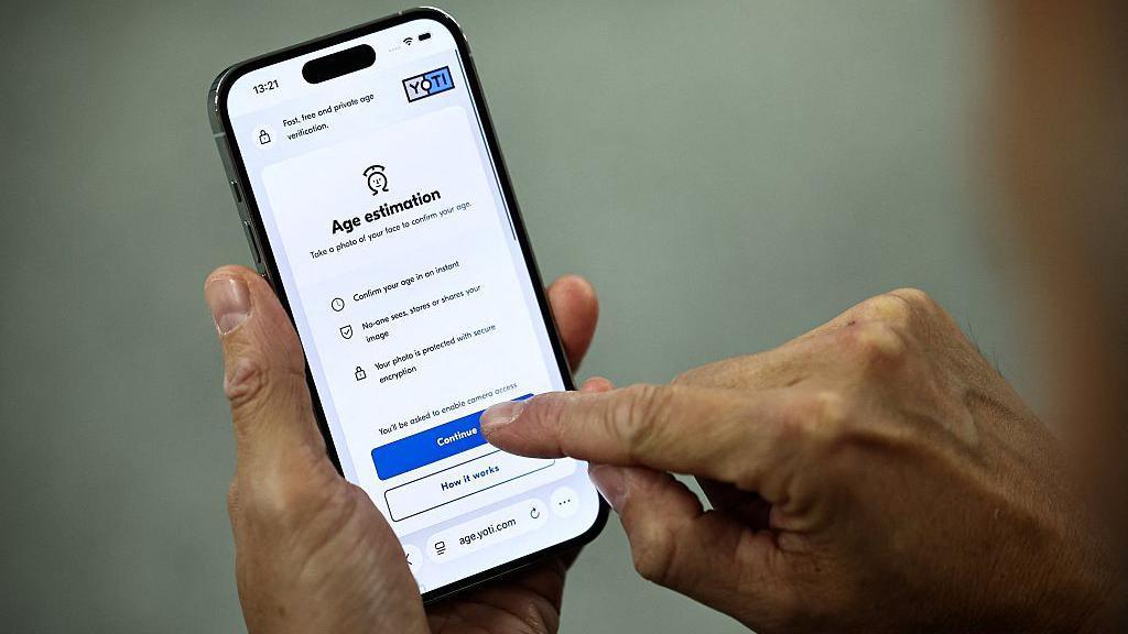 A man holds a phone showing how to sit an age estimation check from the company Yoti
