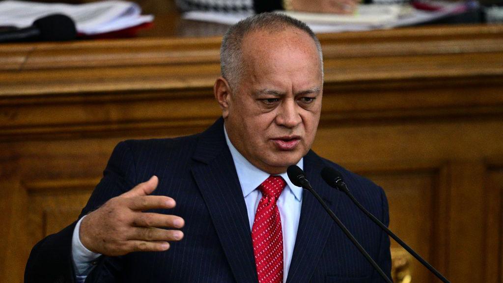 Venezuela's interior minister Diosdado Cabello stands before a microphone, wearing a dark suit, white dress shirt and red tie, his right hand raised as he speaks before the Venezuelan parliament