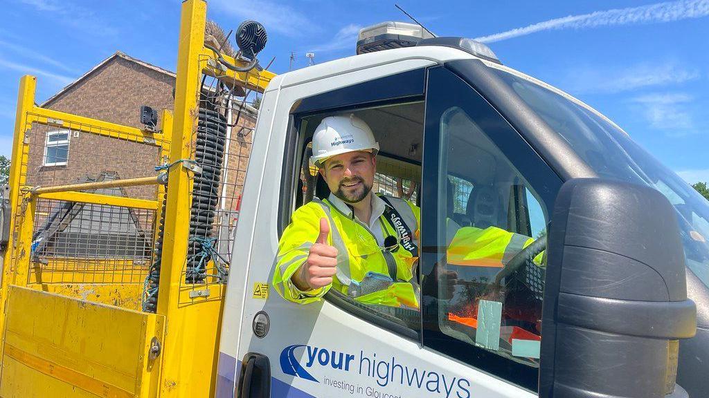 Highways maintenance and communications cabinet member Joe Harris pictured in the driver's seat of a council highways van. He is wearing Hi-vis and hs hi thumb up whilst smiling.