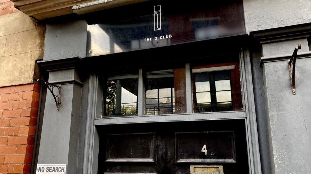 The door of The I Club in Nottingham. The doors are black with glass panels above. A sign above the door says The I Club with a logo above it.