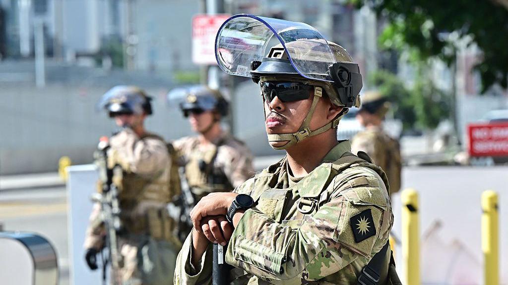 California National Guard troops standing in Los Angeles on 17 June, 2025. There is one in the foreground with his visor up and three in the background.