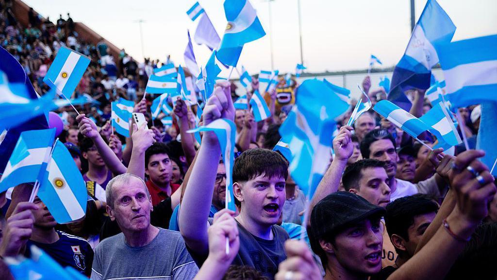 Supporters of President of Argentina Javier Milei wave Argentine flags waiting for his arrival at a closing campaign rally ahead the mid-term election on October 23, 2025 in Rosario, Argentina