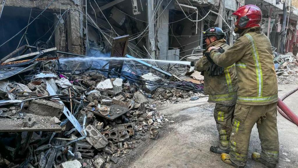 Emergency workers putting out a fire with a hose following an Israeli strike in southern Beirut