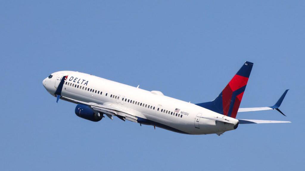 White plane with Delta airlines logo flies through a completely blue sky