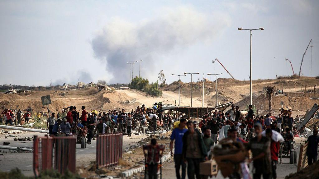 A plume of smoke rises in the background as Palestinians return from a food distribution point run by the US and Israeli-backed Gaza Humanitarian Foundation (GHF) group. 