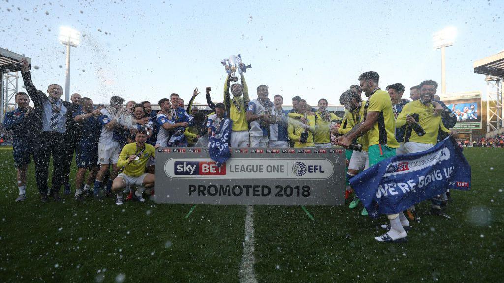 Blackburn Rovers players and staff celebrate promotion on the pitch.