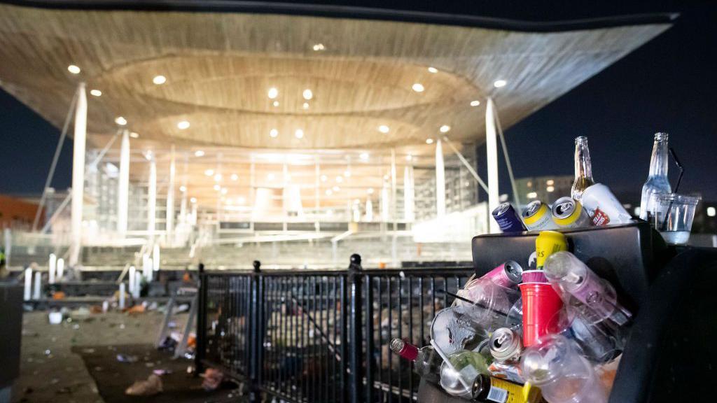 Senedd Cymru yn y cefndir, a bin sbwriel orlawn yn agosach at y camera 