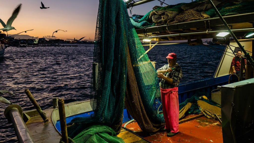 A fisherman is repairing nets after trawling in the Port of Molfetta, Italy