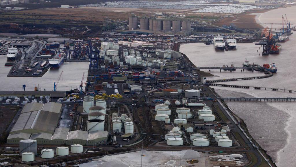 An aerial view of a biodiesel plant with a big area of water and circular buildings next to the beach and shoreline. 
