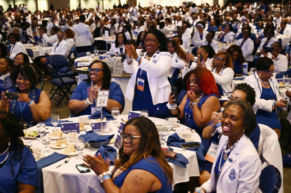 Black women dress in blue and white smile and applaud in an event room