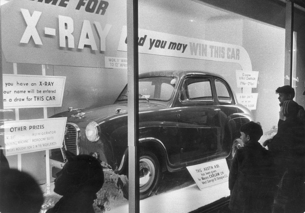 A window display with an Austin A35 car and a sign reading 'if you have an x-ray your name will be entered in a draw for this car'