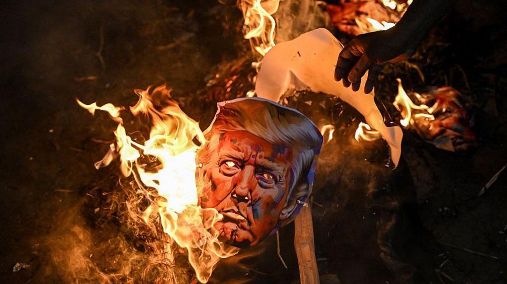 A burnt effigy of US President Donald Trump seen with flaming embers. Activists from different unions were part of a protest against the tariff hikes imposed by the US on India during a demonstration in Kolkata on August 13, 2025.