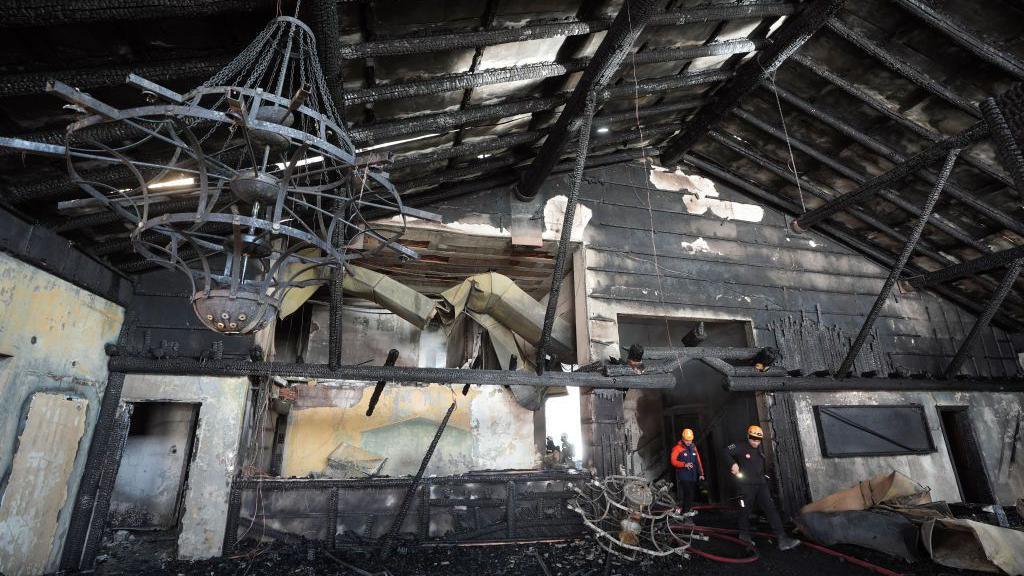 Two firefighters walk through a blackened, fire-damaged room in a hotel in the Bolu Kartalkaya Ski Resort in Turkey