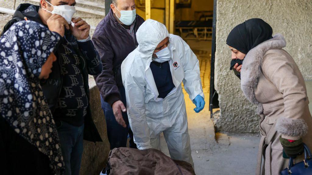 A woman covers her mouth as she is shown the body of a man at a hospital in Damascus, after rebels said they had found around 40 showing signs of torture at Harasta hospital (10 December 2024)