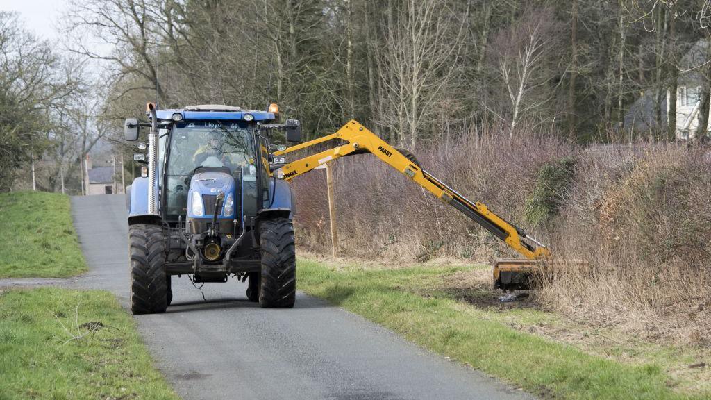 A tractor cuts grass verges along a rural road.