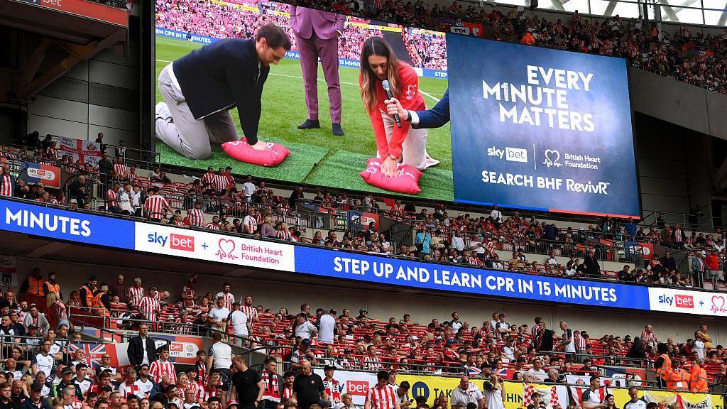 Tom Lockyer performs a CPR technique demonstration on the LED screen at half-time during the Championship play-off final match between Sheffield United and Sunderland at Wembley Stadium.