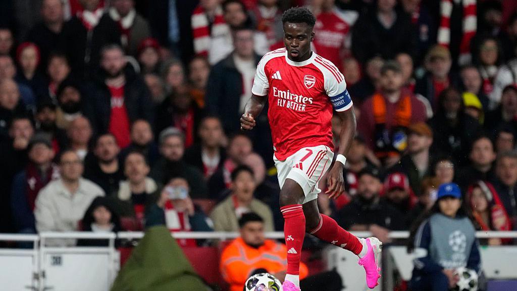 bakayo saka dribbling the ball with the stadium crowd out of focus behind him