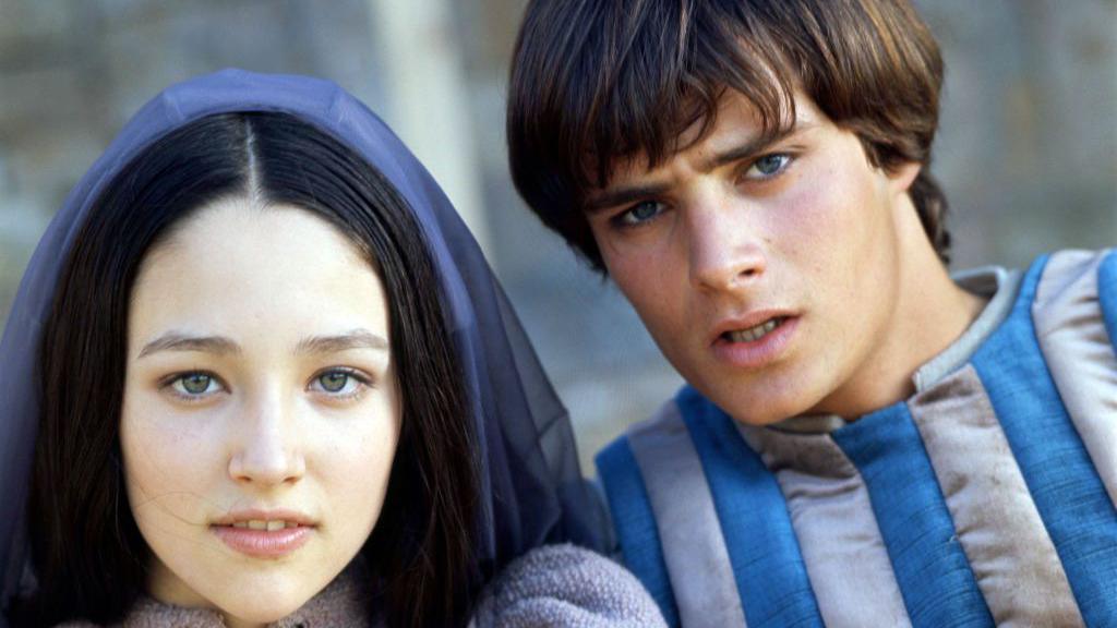 Leonard Whiting, as Romeo, and Olivia Hussey as Juliet in Romeo and Juliet. Both are in costume - she is wearing a blue knitted top and a blue headscarf and he is wearing a blue-and-grey vertical striped top. 