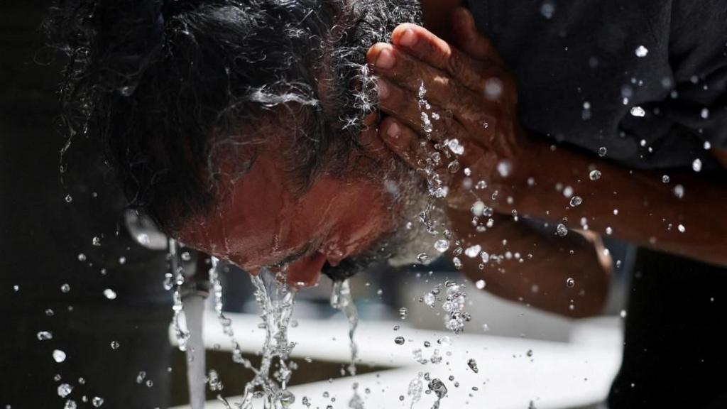 A man washes his face to cool off during a hot day amid a heatwave