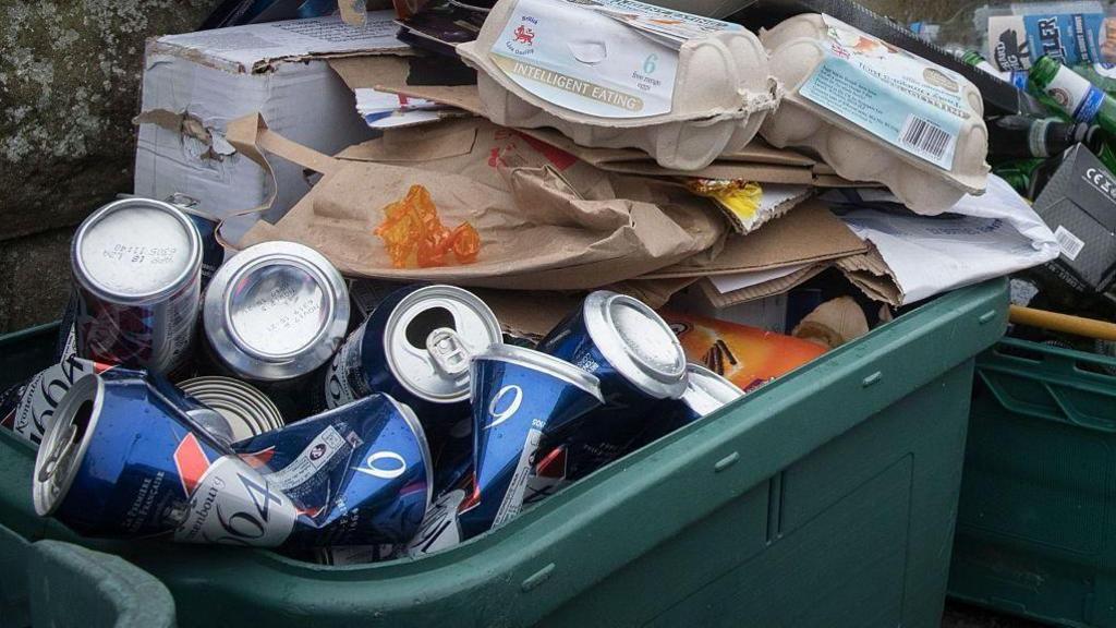 A full green recycling box on a street outside