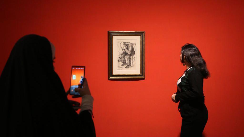 A woman looks at a Van Gogh artwork on display on a red wall