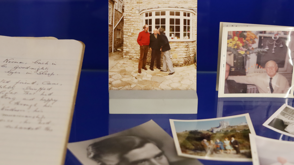 A display of photographs and a notebook. The photograph in the centre shows Brynley kissing Notley on the cheek in the street while standing alongside another man.