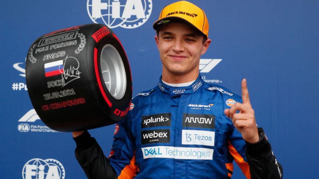 Lando Norris holds the pole position trophy and raises his left index finger in celebration at the 2021 Russian Grand Prix