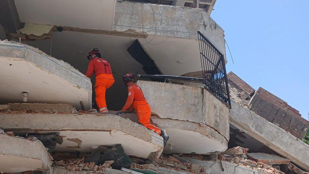 Two firefighters in orange uniforms climbing the rubble of a damaged building. 