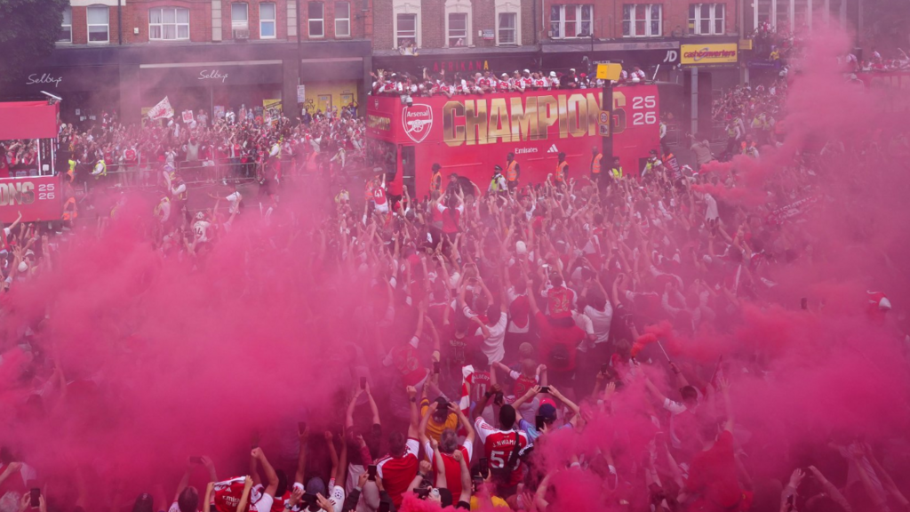 Arsenal bus surrounded by fans as it drives down the victory parade route. Red smoke from flares clouds the large crowd