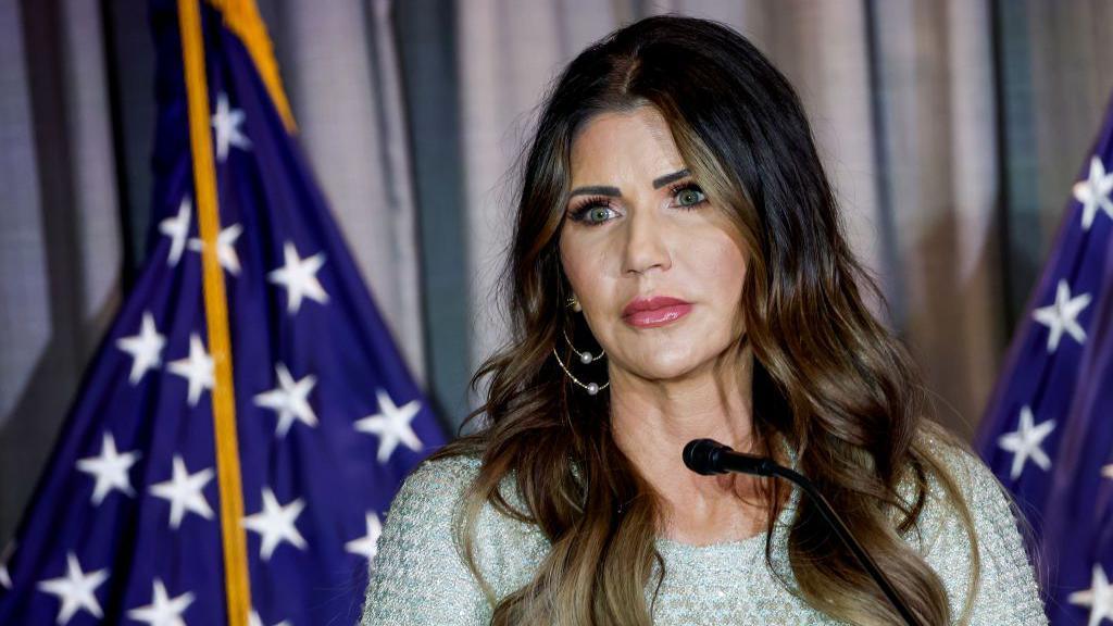 Kristi Noem, wearing a silvery-white dress, looks out during a speech at the Calvin Coolidge Foundation conference 