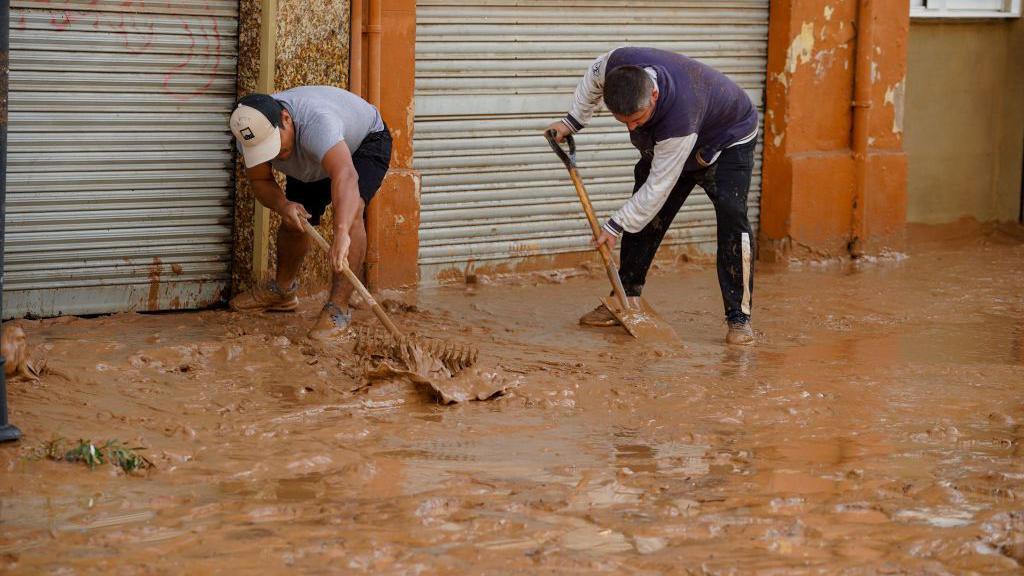 Residents in Valencia attempt to clear the road after flooding 