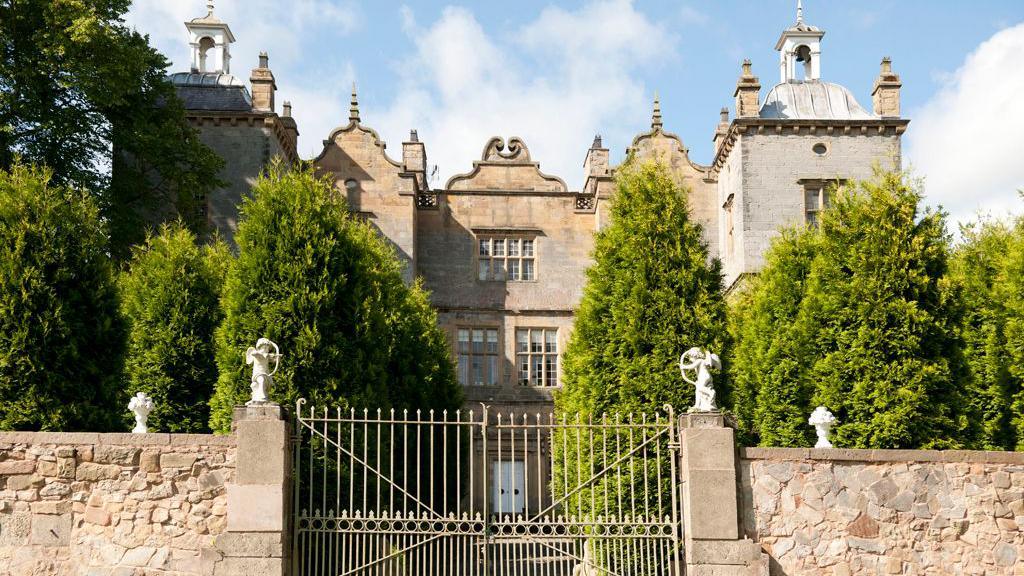 Plas Teg, constructed from grey sandstone, behind iron gates and a walled garden.  