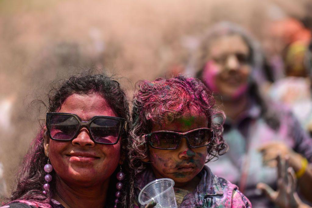 A woman and a child covered in paint and wearing sunglasses look at the camera.