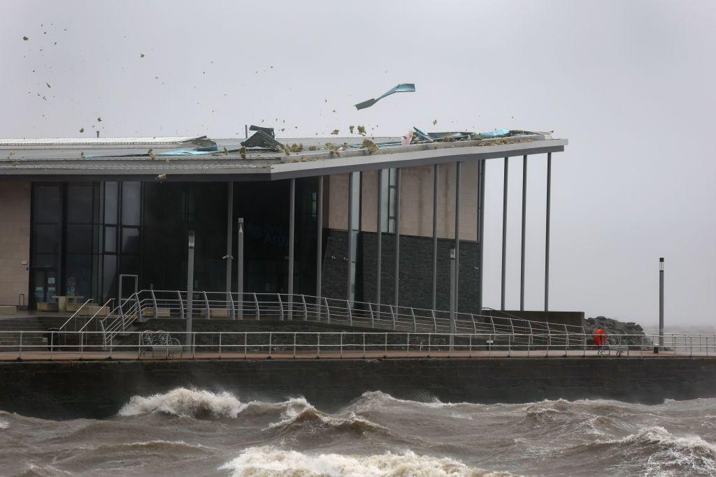 A swimming pool building next to the coast. Part of the roof has blown off due to high winds