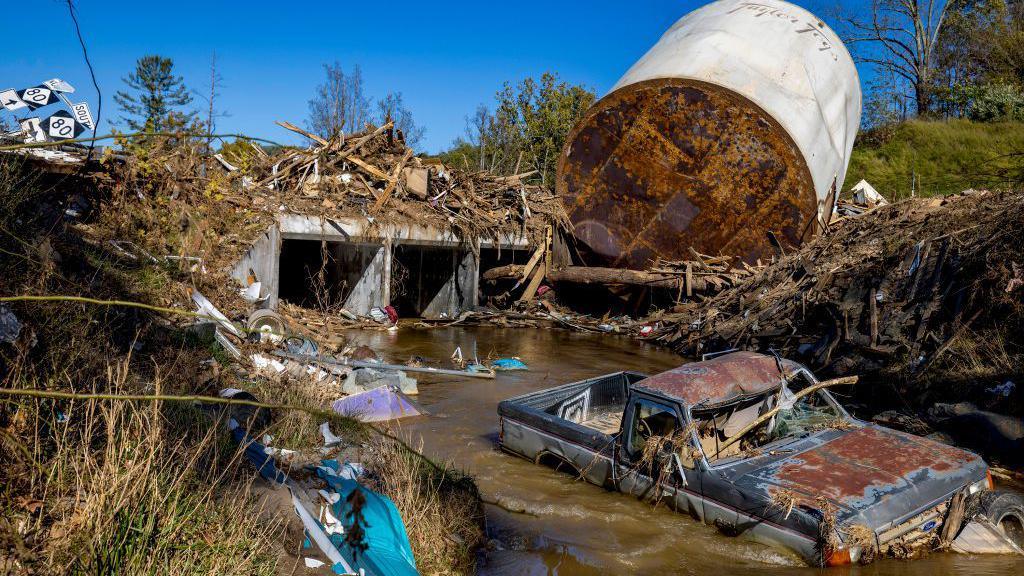 A car sits in a creek and a structure is overturned after the storm Helene, which struck North Carolina and parts of the US south in October 2024.