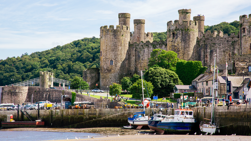 Conwy castle on a sunny day with boats on the beach in front