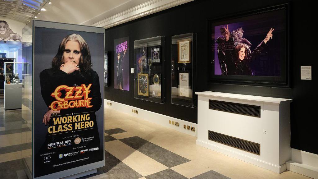 A room showing various framed pictures of Ozzy Osborne. The floor is black and white tiled and the walls are black, with various glass cabinets of pictures of the singer. 