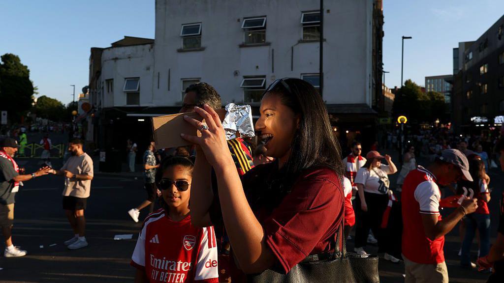 An Arsenal fan uses tin foil and a cardboard box to try and see the solar eclipse prior