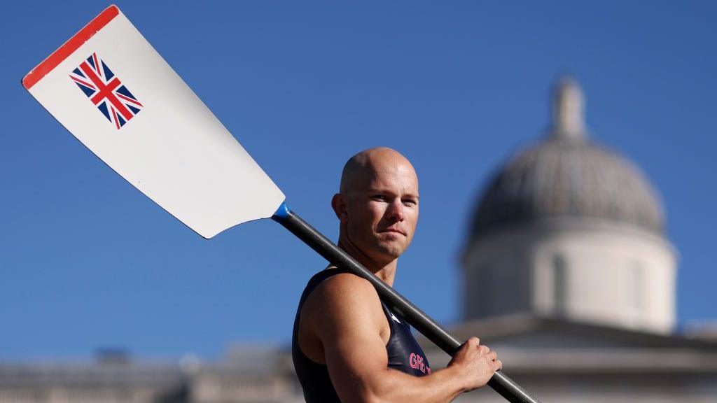 Sam Murray holding an oar over his shoulder, which has a Union Jack on it