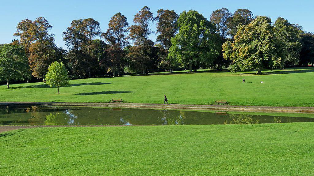 A wide angle view of Abington Park on a sunny day. There are tress in the background and a lake in the foreground