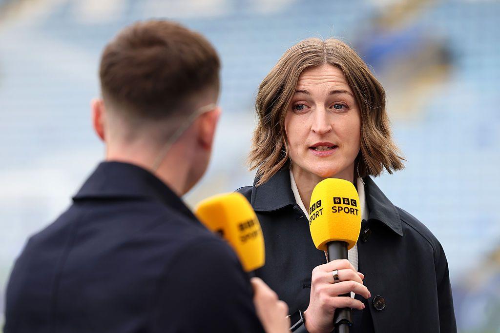 Ellen seen with dark hair in a middle parting. She is holding a yellow microphone branded with the BBC Sport logo