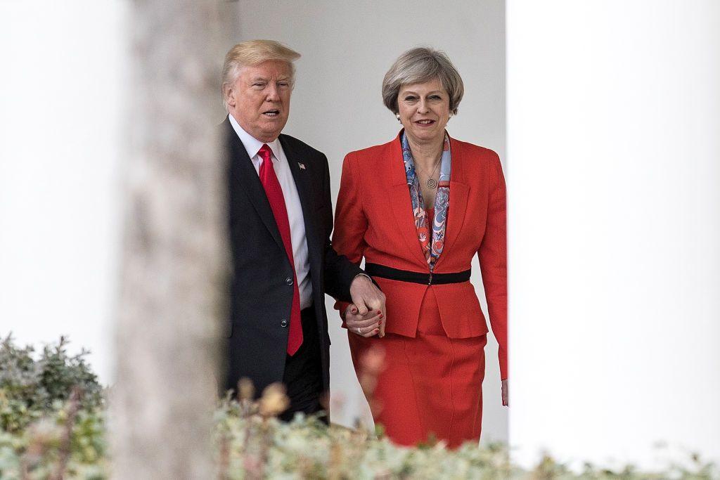 Theresa May, dressed in red, holds Trump's hand as they walk by the White House.