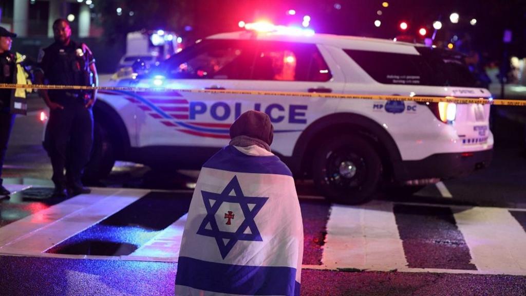 A man wrapped in an Israeli flag sits opposite a police car